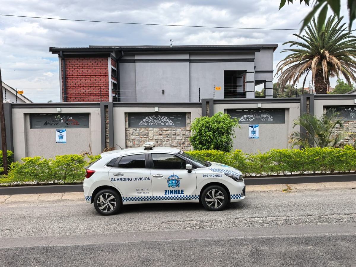 A white Zinhle Guarding Division reaction vehicle with the phone number 010 110 0533 on its door, parked in front of a home.