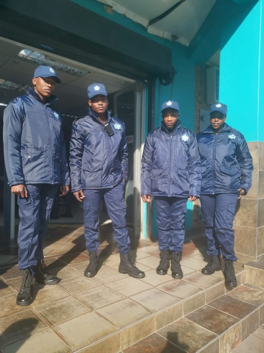 Four Zinhle security officers in navy jackets and caps standing at a shop entrance.